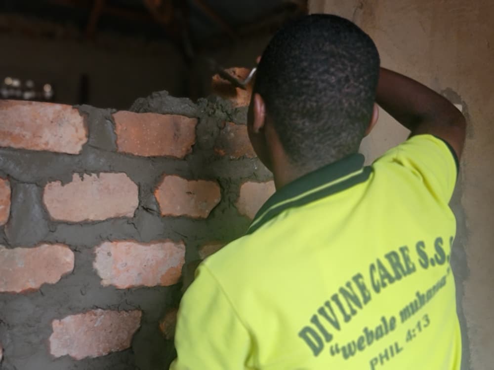 A student in a Divine Care work suit laying bricks during practical training